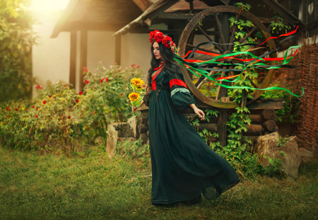 Fantasy portrait Ukrainian happy authentic woman walks in motion. Long brunette hair. Ribbon silk fabric flying in wind waving. Art photo levitation. National black dress. Wreath red crown flowersの写真素材
