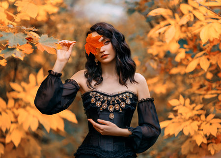 Fantasy woman princess holds red orange autumn fallen maple leaf in hands hides face. Sexy dark queen girl looks at camera. black gothic vintage dress. Yellow nature foliage trees. Art photo portraitの写真素材