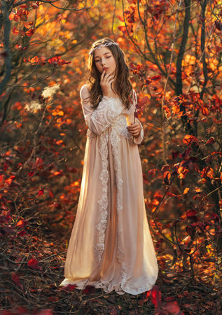 Fantasy portrait teenage princess girl walking in forest, blond flowing hair cute face. White vintage dress, silver crown diadem on head. Autumn nature red orange leaves trees. Elf nymph young womanの写真素材