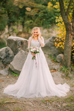happy bride woman holding wedding creative bouquet white purple rose flowers berries eucalyptus plant bridal long white lush dress Girl blonde hair smiling face. autumn nature forest green trees.の写真素材