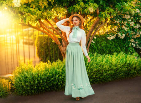 Art Fantasy young woman in vintage straw hat on head walking in garden, girl princess pretty face red hair, retro old style white blouse mint skirt, bow tie. green grass yellow sun light summer natureの写真素材