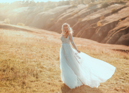 happy beautiful joyful bride is dancing spinning having fun, wedding long gray-blue light dress flies waving in wind blow motion. Girl blonde hair smiling face. autumn nature divine magic sun light.の写真素材