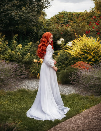 Fantasy photo red-haired woman walks in summer blooming garden Long flowing red hair white vintage old historical style dress hem train. Girl sexy aristocrat back rear view leaves. Green nature treesの写真素材