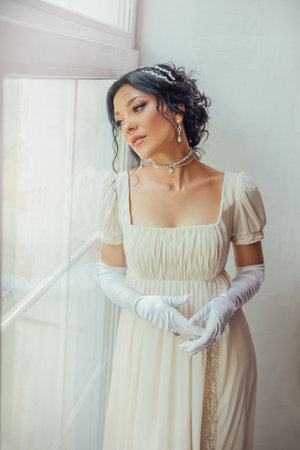 art photo real person fantasy portrait beautiful woman standing by window, white dress vintage old style. Sexy lady girl waiting love. dark hair hairstyle, evening make-up face lips eyes 19th century.の写真素材