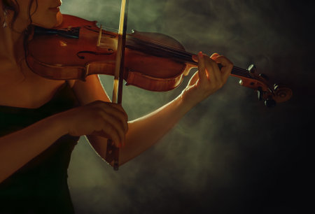 Art photo real person close-up lips, hand body part woman violinist cropped face musician plays music on the violin holding in hands musical instrument. Girl in black studio full smoke light dark roomの写真素材