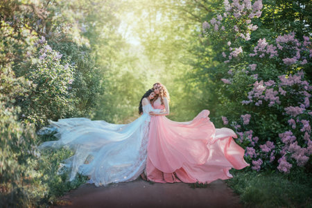 portrait two girls princesses lie in green grass blooming purple flowers. Woman dream beautiful face closed eyes, two friends enjoy nature spring summer aroma. Curly long healthy hair brunette blondeの写真素材