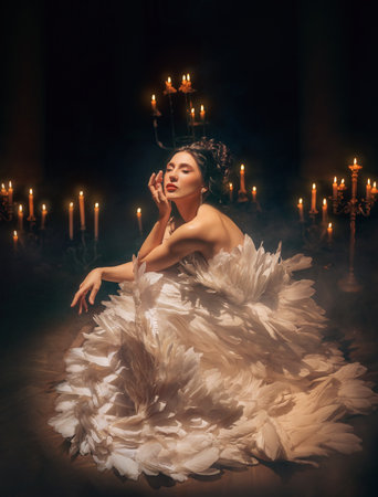 art photo real person girl princess sitting surrounded by candles light flame in dark room old style. Fantasy woman bird beauty face make-up black hair. white dress like flower natural feathersの写真素材