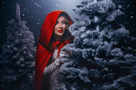 Portrait happy woman hiding behind tree, looking around in dark night forest winter nature snow falling fog, fairy tale Fantasy girl princess beauty face lips eyes red hood on head cape white dressの写真素材