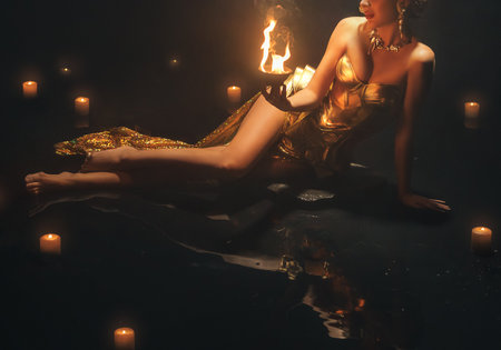 art photo real person Fantasy goddess Beauty woman fashion model in metal fabric golden shiny dress, fairy mystery girl hands holding burning fire flame, dark black water night river, magic light skyの写真素材