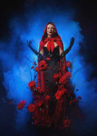 art photo real person gothic sexy woman queen walking in fairy tale dark night garden roses flowers bush tree hands raised to sky. Fantasy lady girl long cape dress red hood on head. blue moon lightの写真素材