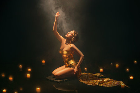 art photo real person Beauty woman fashion model hand raised to divine light from night sky in dark black water smoke fog, magic candles burning, blonde hair girl body. fantasy golden shiny dressの写真素材
