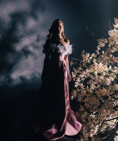 art photo real person fantasy woman walking through branches in light ray in black night dark forest fog tree white flowers blooming tree. lady fairy elf Girl blond fashion modelの写真素材