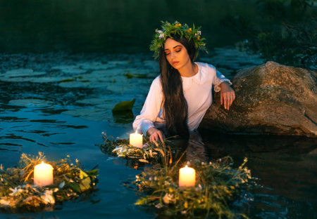 Slavic woman nymph stands in water herbal wreath floa candles burning. Fantasy girl mermaid. White long wet dress. Summer night green grass tree river. pagan holiday Ivan Kupala divination maidensの写真素材