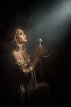 fantasy woman queen queen praying hands folded in prayer holding sword girl kneeling in dark room castle looking at ray of light hope. Black night white dress. Elf girl warrior on knees. sharp bladeの写真素材