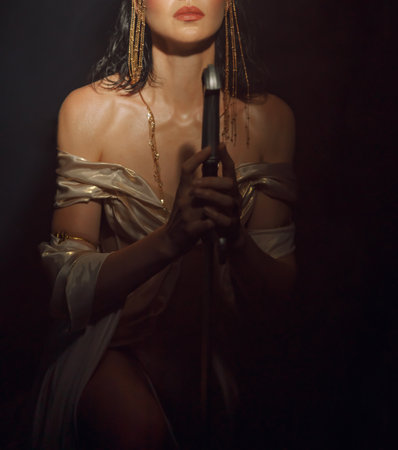 art photo cropped face lips close-up fantasy woman queen praying hands folded in prayer holding weapon sword girl in dark night room. white golden sexy dress. Elf princess girl warrior on knees poseの写真素材