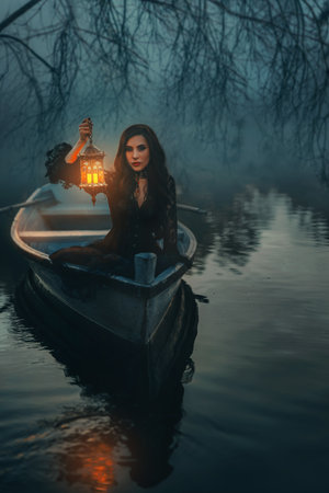 photo real person fantasy gothic woman floating in boat down river night nature, hand holding lantern with warm light. Mystery girl in ship along lake in fog twilight, dark forest trees. Black dressの写真素材