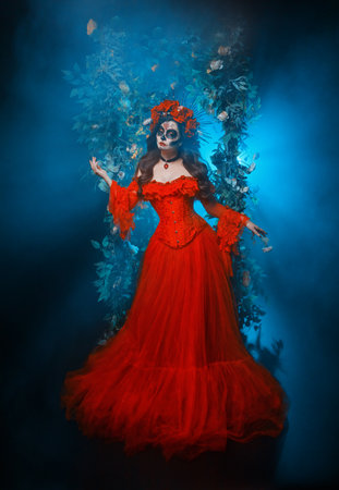 beauty face woman sugar skull make-up eyes lips art paint, long vintage style red dress crown with roses flowers on head. Girl Calavera goddess of death in dark black night garden arch trees fogの写真素材