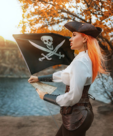 Art photo real person fantasy woman captain pirate holding in hands map searching for treasure looking for wealth. Fairy tale girl thief game old style costume. black pirate flag fly flutters in windの写真素材