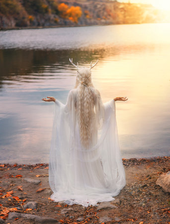 art photo real person, faerie fantasy woman is praying hands raised to sky by river lake water nature. sexy fairy tale elf girl long blonde hair white dress back, snow queen crown deer antlers on headの写真素材