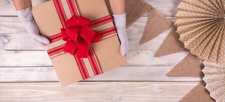 Safe celebration party. Hands holding red gift ribbon box with rubber gloves, over wooden background. Top viewの写真素材
