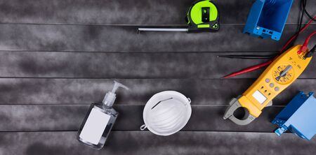 Professional electrician emergency and repair services. face mask, hands sanitizer, multimeter and space for text in a wood background.  Social distancing.の写真素材