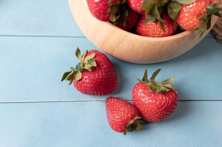 Juicy and fresh organic strawberries in a bowl and some part on a blue wood background. Concept for healthy nutrition. Close up view. Copy space.の写真素材