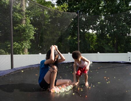 siblings playing outside with water  balloons in the summer on trampoline.