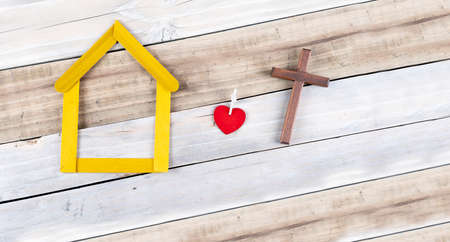 Heart and Wooden cross next to small yellow house wooden on white background. religion lifestyle concept. copy spaceの写真素材