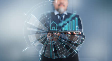 A businessman using digital tablet with house icon, data and business growth on hologram. Futuristic technology style, on blue background.の写真素材