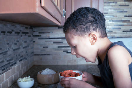 Close-up of kid eating ingredients for home made pizza in the kitchen. copy space.の写真素材