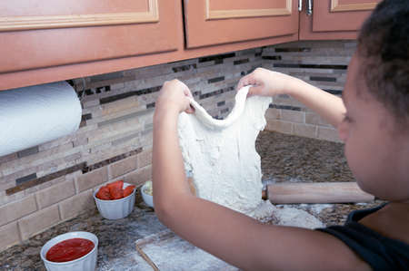 Close-up of boy hands preparing dough for pizza with flour and rolling pin on wooden background....