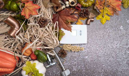 White thermostat and construction tools on autumn background with maple leaves and pumpkin....