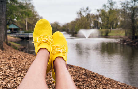 Cropped image of woman legs relaxing outdoors in wearing sneakers yellow.
