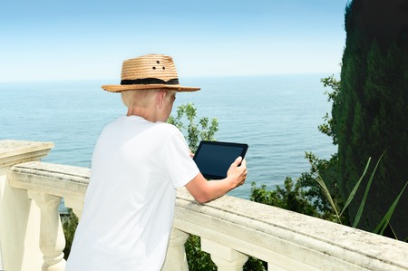 Boy costs against the background of the sea and using the tabletの写真素材