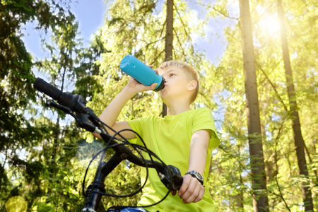 Happy teenager rides a bicycle in pine wood, in sunny day.の写真素材