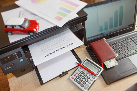Homeowner and car Insurance form with Laptop, Printer, pen, dollars, calculator on the table....