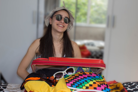 Girl packing bag for travel, closing hardly overfilled luggage bag. Good day for a journeyの写真素材