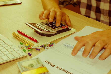 Businessman working on office desk with Calculator. accounting concept. Financial report values with dollars, calculator - Retro colorの写真素材
