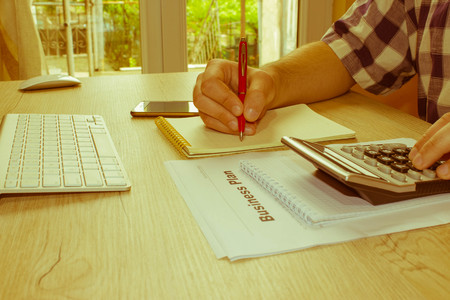 The Man and computer are using a calculator on the table in the office room. accounting and business concept. The Man sits at the table with a computer and business accessories - Retro colorの写真素材