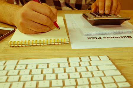 Businessman hand using calculator, accounting concept. Man hands with pencil, notebook and Calculator on wooden table - Retro colorの写真素材
