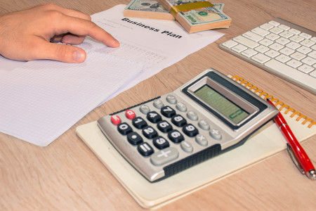 Close up view of bookkeeper or financial inspector hands making report, calculating or checking balance. Business plan, calculator, dollar banknote on the tableの写真素材