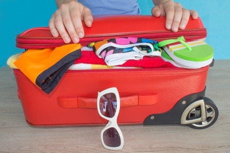 Woman hands packing her red suitcase. Travel and vacations concept. Open traveler's bag with clothing, accessoriesの写真素材