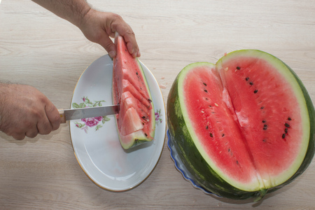 Summer and fresh watermelon topic: human hand with a knife beginning to cut a watermelon. watermelon and Male hands on tableの写真素材