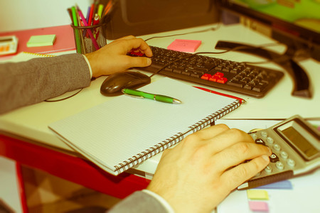 closeup pen on paperwork accounts with man use computer to save data in background. accounting concept. Man hand with pen, calculator and computer on wooden table - Retro colorの写真素材