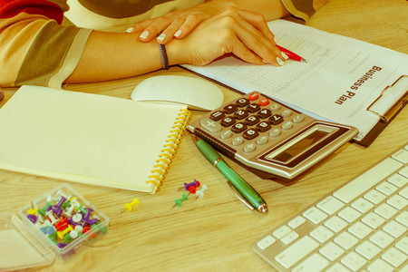 Female with Business plan, calculator and pen on the table. Young woman working in office, sitting...