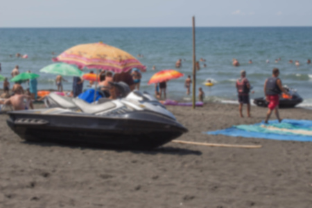 Blurred background photo of people on the beach having fun under umbrellas. Water scooter on the...