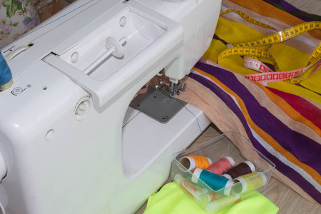 woman's hands using sewing machine with reels of colour threads. Workplace of tailor. people,...