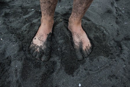 Bare feet of a wet girl in black sand on beach. Travel or sea vacations conceptの写真素材