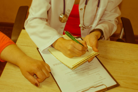Doctor is talking with female patient and making notes while sitting in his office. Health care - Retro colorの写真素材