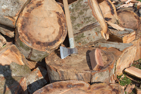 Old axe standing against a piled pieces of firewood. Preparing firewood. Chopping wood for fuel
